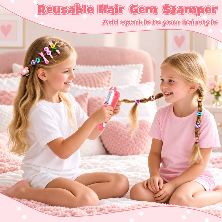 Two young girls sitting on a pink bed in a bedroom setting, demonstrating a reusable hair gem stamper. One girl holds a pink stamping tool with colorful hair gems, while the other has a braid decorated with matching colorful hair gems.