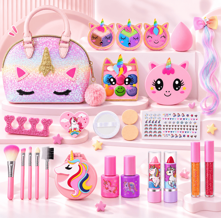 A pink unicorn-themed makeup and accessory set arranged on white display steps. The set includes a glittery unicorn handbag, makeup brushes, nail polish bottles, lip gloss tubes, a face palette, stickers, a pom-pom, and other small beauty accessories in pastel pink, purple, and rainbow colors.