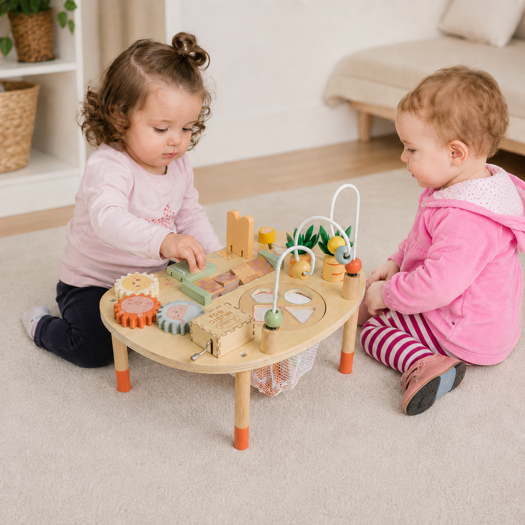 Two toddlers sitting on a beige carpet, playing with a small wooden activity table set in a bright, modern nursery.